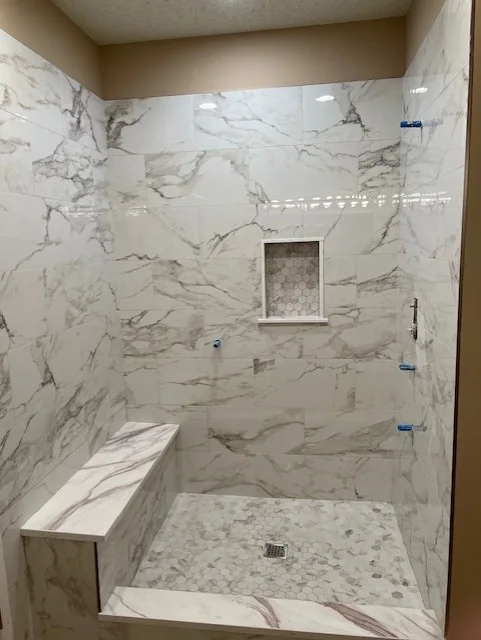 Marble-look shower tile installation with a built-in bench and recessed niche